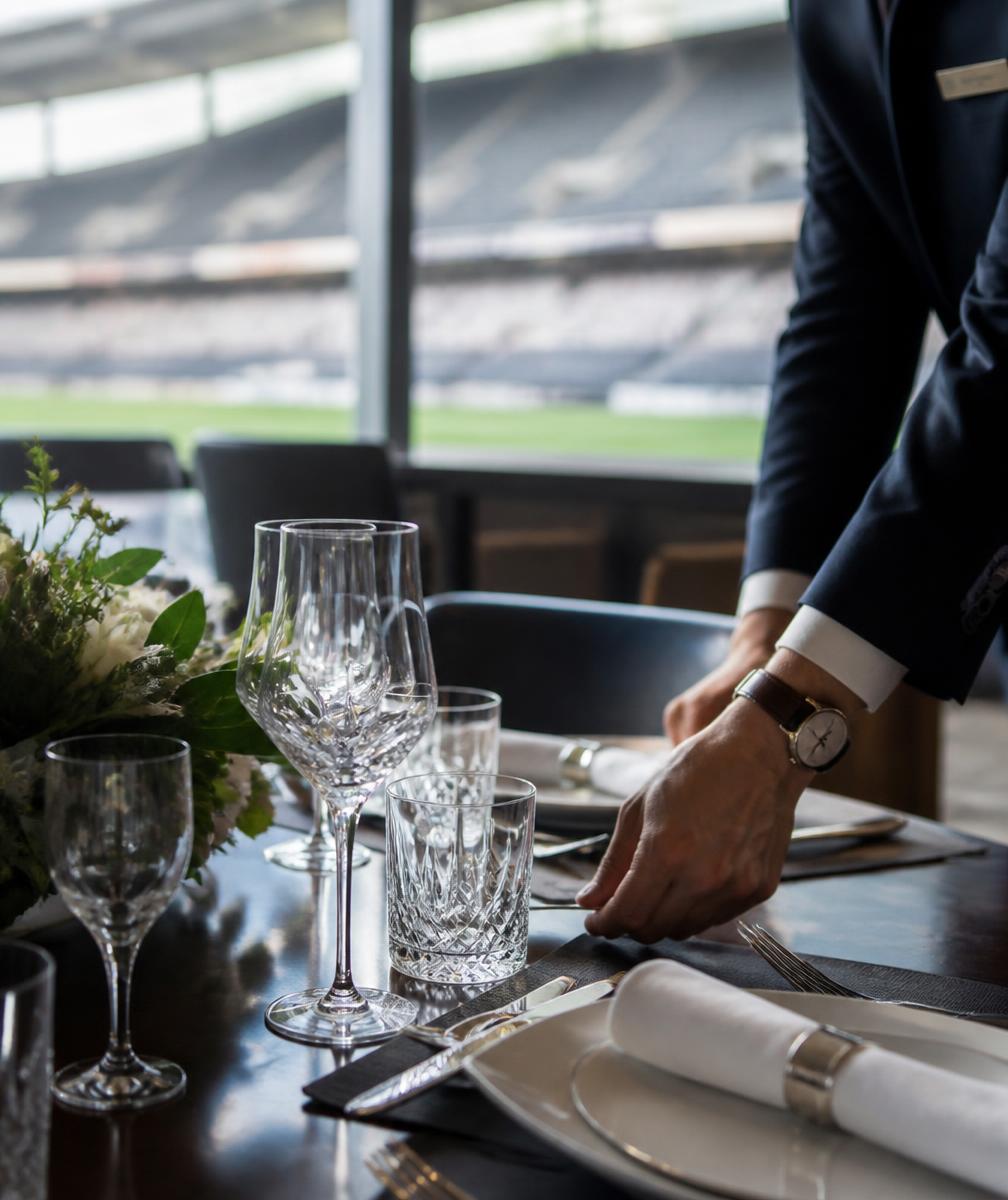 A hospitality suite table being set with glassware above a stadium pitch